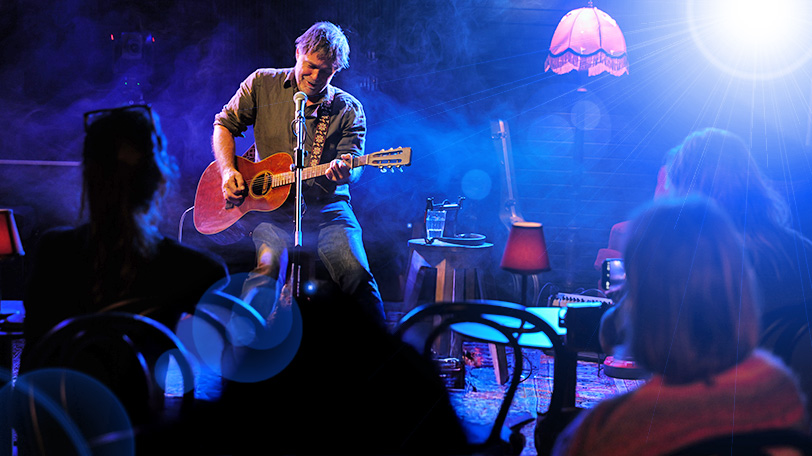 THE SESSIONS — performer playing guitar and singing in front of small audience